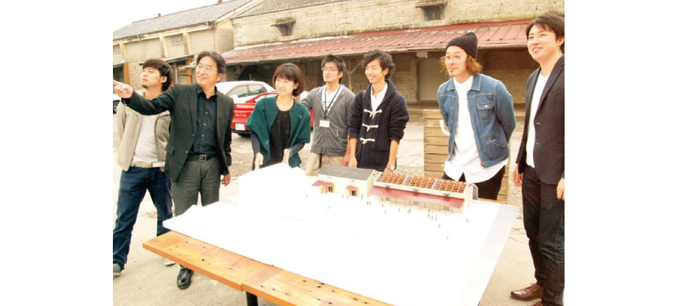 既存施設模型を囲むプロジェクトメンバー（撮影：慶野正司）プロジェクトに参画した地元建築学生が<br />
作成した吉田村village中心施設エリアの既存全体模型と囲むプロジェクトメンバー（一部）。